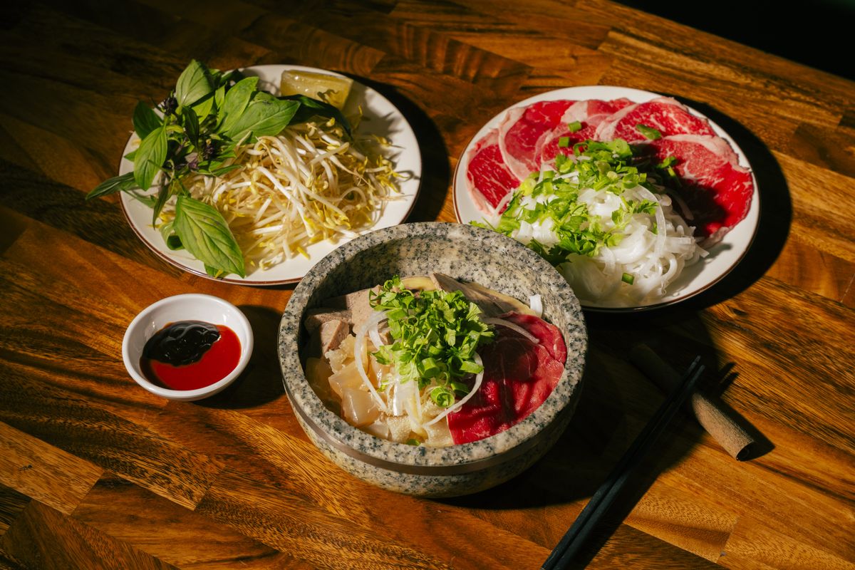 A Bà Năm phở spread — stone-bowl pho with rare beef, fresh herbs and bean sprouts